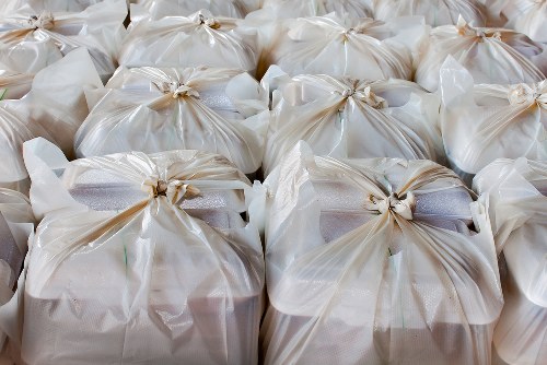 A large number of tightly packed white plastic rubbish bags, each secured with a twist tie or knot, are arranged in neat rows on a paved surface, likely for disposal or collection in Rotherhithe. The bags appear to contain household or office waste, with some showing slight bulges and creases indicating fullness. The background does not reveal additional surroundings but focuses solely on the uniform display of waste bags, typical of a rubbish removal or clearance operation conducted by Office Clearance Rotherhithe. The scene emphasizes the bulk nature of waste management tasks, with the bags on a flat, outdoor surface, possibly near a building or parking area, prepared for pickup. The lighting is natural, highlighting the glossy finish of the plastic and the subtle shadows created by the bags’ gathered tops, illustrating a typical environment where rubbish collection services are engaged to clear accumulated waste efficiently and systematically.