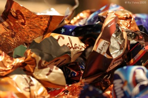 A close-up photograph of a pile of crumpled metallic and plastic wrappers, predominantly in shades of copper, blue, silver, and black, with some colorful patterned designs visible. The wrappers appear glossy and reflective, highlighting their crinkled textures. The background is indistinct, focusing attention on the scattered rubbish. The image likely depicts discarded packaging material, often associated with rubbish removal services in urban or suburban areas such as Rotherhithe, where office clearance tasks may involve clearing such waste from commercial or residential settings. The detailed visual rendering emphasizes the different materials and textures of the waste, illustrating the type of refuse handled by Office Clearance Rotherhithe, specialised in rubbish clearance tasks within the local postcode area. This depiction supports the understanding of typical rubbish items requiring professional removal in the local community without including any identifiable individuals or extraneous environment details.