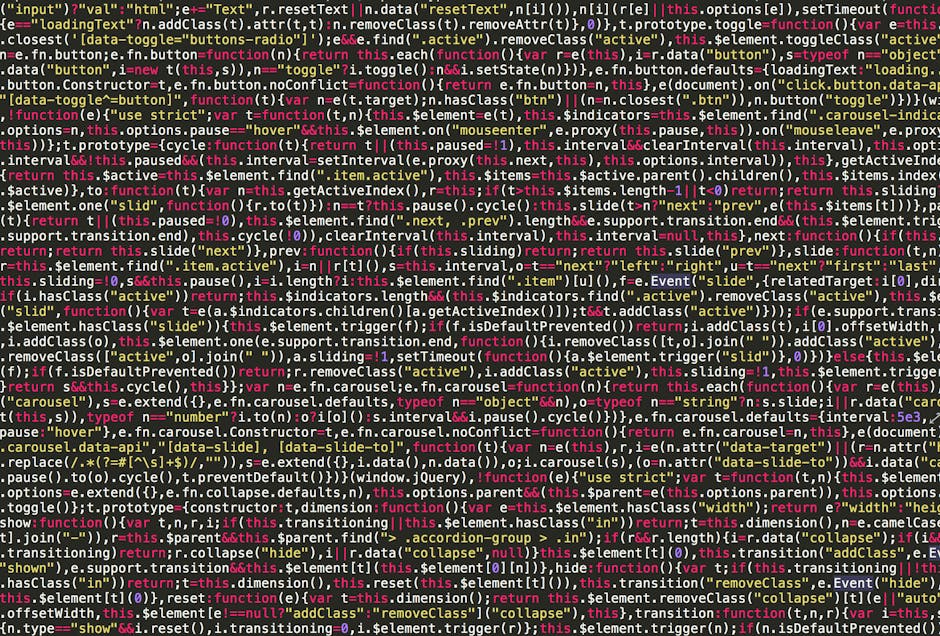 A close-up view of a black laptop with a red-backlit keyboard, displaying lines of colorful, blurred programming code on its screen, positioned on a dark surface. Next to the laptop, there is a white